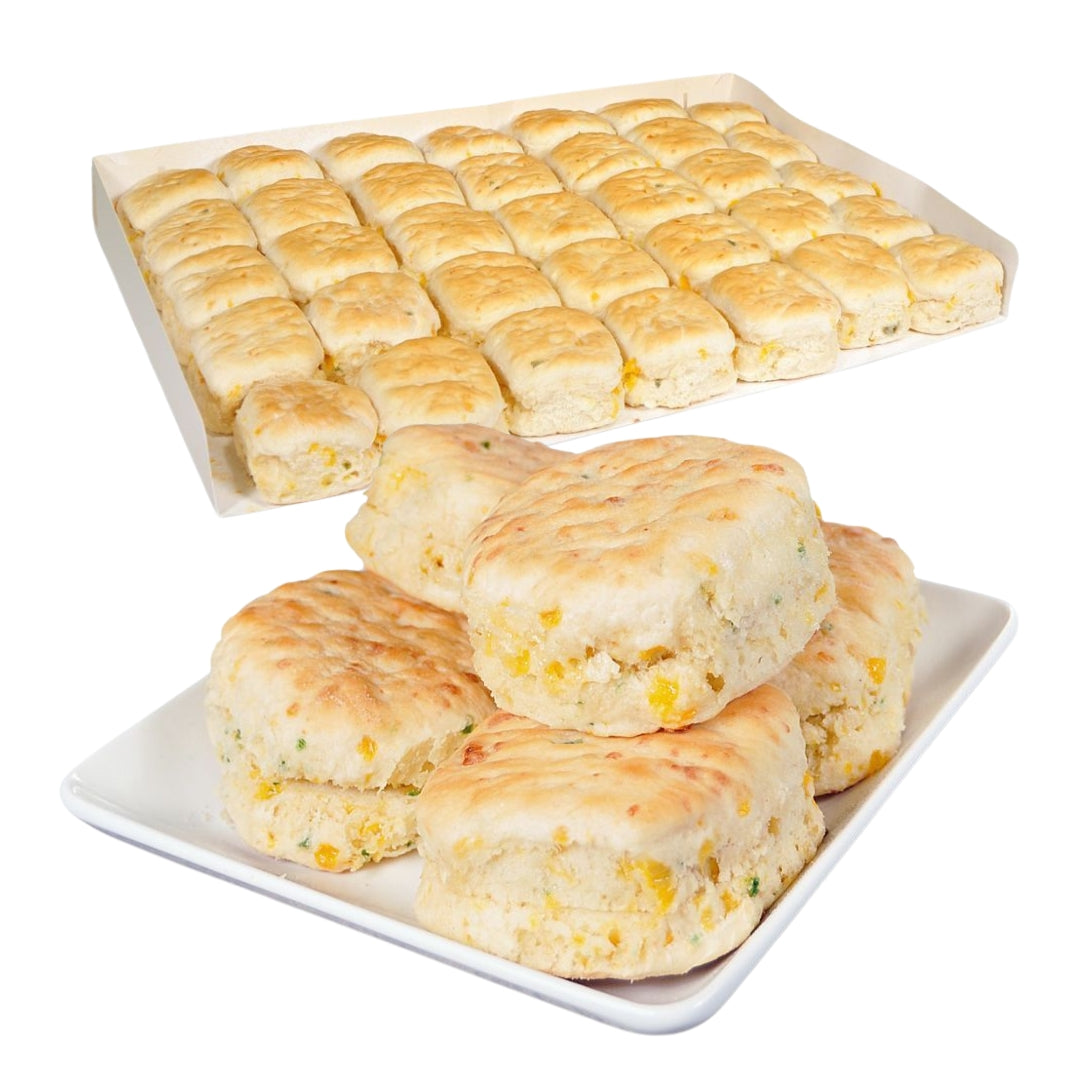 Golden-brown Bridgford cheesy jalapeño biscuits stacked on a plate in front of a bulk tray of baked biscuits.