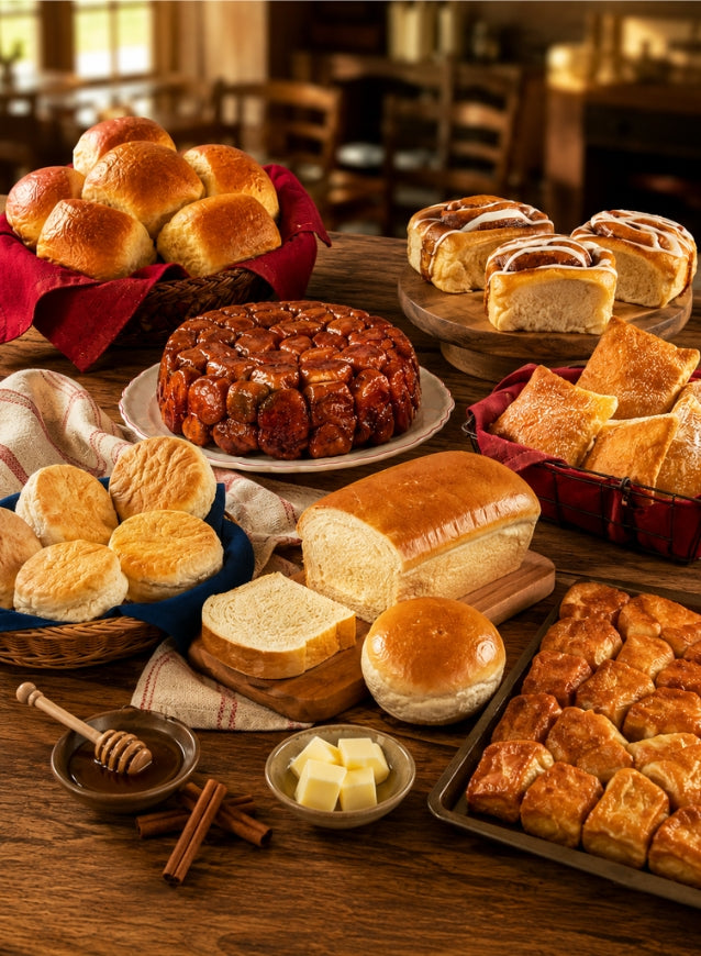 Large spread of freshly baked Bridgford bakery items including rolls, biscuits, bread, cinnamon rolls, and monkey bread.